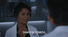 a woman in a lab coat with the name tamlyn tomita