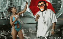 a woman in a bikini is holding a bunch of money next to a man with a monkey head on his head