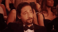 a man in a tuxedo and bow tie is crying while sitting in a theatre .