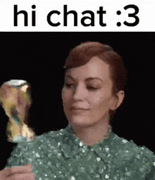 a woman in a green dress is holding a trophy and says hi chat : 3 .