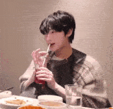 a young man is drinking a drink through a straw while sitting at a table with plates of food .