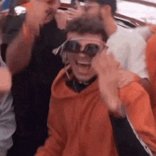 a man wearing sunglasses and headphones is laughing while sitting in a crowd of people .