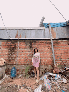 a girl in a pink skirt stands in front of a brick wall and a pile of trash
