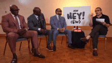 a group of men sitting in front of a sign that says hey