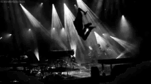 a black and white photo of a person jumping in the air on a stage at a concert .