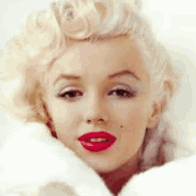 a close up of a woman 's face with red lips and a white fur coat .