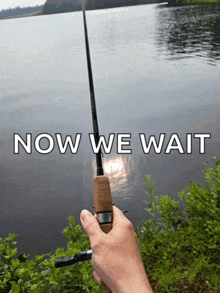 a person is holding a fishing rod in front of a lake with the words now we wait above it