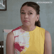 a woman wearing a yellow and pink tie dye dress is sitting in front of a white chair