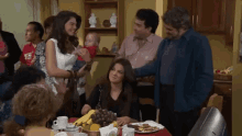 a group of people are gathered around a table with a woman holding a baby in her arms