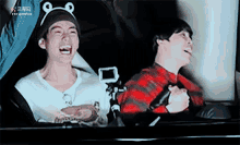 a man wearing a frog hat is laughing next to another man wearing a plaid shirt