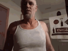 a man in a white tank top stands in front of a coca-cola bag