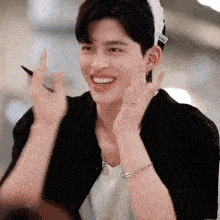 a young man wearing a hat and a bracelet is smiling and making a peace sign .