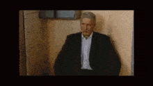 a man in a suit and tie is sitting in a bathroom .
