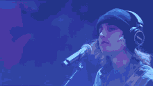 a man wearing headphones and a beanie sings into a microphone