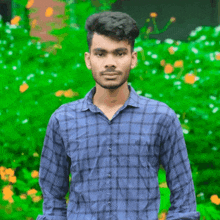 a young man wearing a blue plaid shirt stands in front of a green background