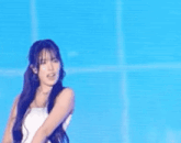a woman with long blue hair is standing on a stage in front of a blue background .