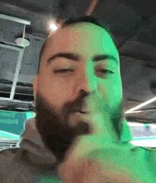 a man with a beard is smoking a cigarette in a dark room with green lights .