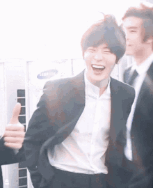 a man in a suit giving a thumbs up in front of a samsung sign