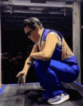 a man in blue overalls squatting on a table