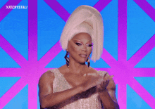 a drag queen is clapping her hands in front of a blue and purple background