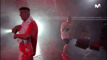 a man in a red shirt is singing into a microphone while another man stands behind him