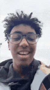 a young man wearing glasses and a hoodie is smiling .