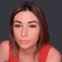 a woman in a red tank top is looking at the camera with a gray background .