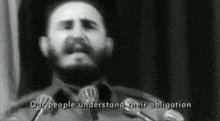 a man with a beard is giving a speech in front of microphones with the words " our people understand their obligation " visible