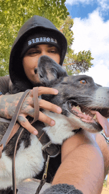 a man wearing a black hat with the word bizzard on it holds a dog