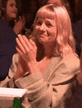 a woman in a green jacket is clapping her hands while sitting in a crowd .