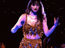 a woman in a gold dress is holding a microphone on stage