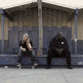 a man on a skateboard sits on a bench next to another man