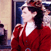 a woman in a red coat and hat stands in front of a yellow building