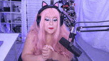 a woman with pink hair and headphones is sitting in front of a microphone .
