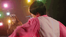 a man in a pink shirt is dancing on a stage with a woman in a fur coat behind him .