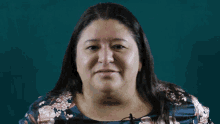 a woman wearing a blue floral shirt is smiling for the camera
