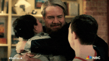 a man with a beard is hugging a woman and a boy with the nbc logo on the bottom