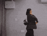 a woman wearing a grey jacket and black pants carrying a black backpack with the letter n on it