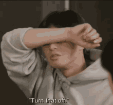 a man in a grey hoodie covering his face with his hand and the words " turn that off " below him
