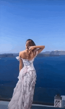 a woman in a long dress is standing in front of a body of water .