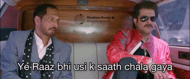 two men are sitting in a car and one of them is wearing a pink jacket