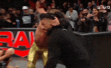 a man in a black hoodie is standing next to a wrestler in a gold outfit .
