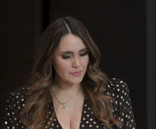 a woman wearing a gold necklace and a black polka dot top
