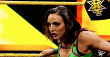 a woman in a green top is standing in a wrestling ring with a x on her shirt .
