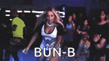 a woman is dancing in front of a group of people and the word bun-b is on the screen .