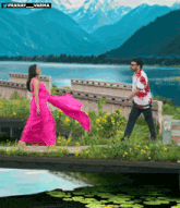 a woman in a pink dress is walking across a bridge with a man in a white shirt