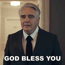 a man in a suit and tie is standing in a hallway and says god bless you