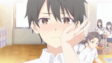 a boy covering his face with his hand in a classroom with other students