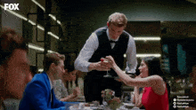 a man in a tuxedo is serving a woman a drink in a restaurant with fox written on the bottom right