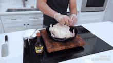 a man is preparing a chicken in a skillet on a stove top with a bottle of marinade next to him